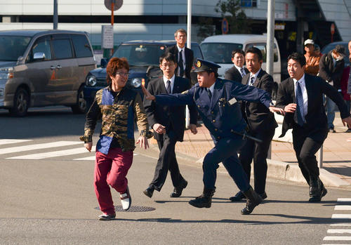 تلاش پلیس ژاپن برای دستگیری یک فرد معترض در مقابل ورودی پایگاه هوایی یوکوتا. این فرد هنگام حضور ترامپ در این پایگاه آمریکایی به نشانه اعتراض قصد ورود به آنجا را داشت.