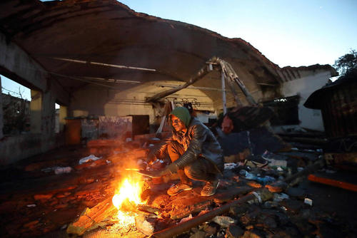 گرم شدن یک پناهجو با آتش در یک مجتمع صنعتی مخروبه در شهر رم ایتالیا