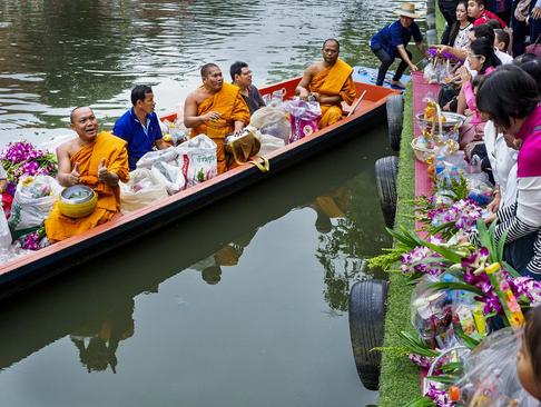 راهبان بودایی تایلندی در یک قایق و در حال جمع‌آوری اعانه از فروشندگان یک بازار شناور در تایلند
