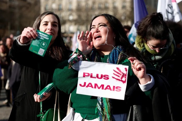 پاریس - تجمع حمایت از اضافه شدن حق سقط جنین به قانون اساسی فرانسه - زنی پلاکاردی در دست دارد که روی آن نوشته شده «دیگر هرگز» در حالی که مردم صفحه نمایش بزرگی را تماشا می کنند که نشان می دهد قانونگذاران فرانسوی در حال جمع شدن برای کنگره ویژه در ورسای برای رأی دادن به لایحه ای برای گنجاندن حق سقط جنین در قانون اساسی هستند [گونزالو فوئنتس/ رویترز]