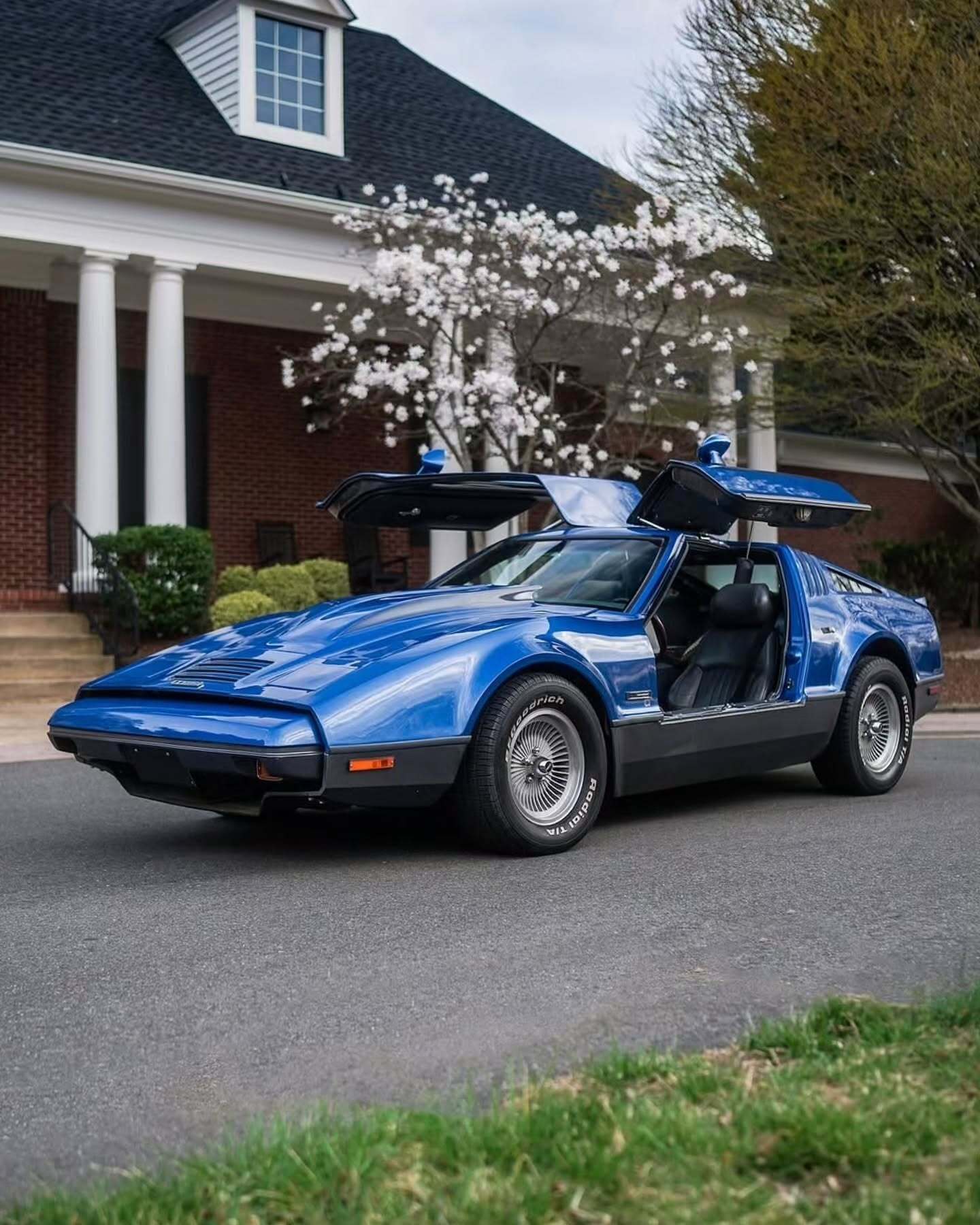 نمای جانبی خودروی کلاسیک بریکلین SV-1 با درهای باز شده رو به بالا و بدنه آکریلیک نارنجی رنگ که طراحی ایمن و آیرودینامیک آن را نشان می‌دهد.