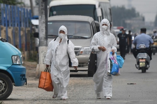 دو زن چینی با لباس‌های محافظت کننده در حال عبور از نزدیکی محله آلوده به ویروس کرونا و قرنطینه شده شهر پکن/ خبرگزاری فرانسه